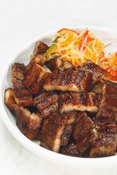 a white bowl filled with meat and coleslaw on top of a table next to a fork