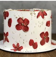 a white cake with red flowers and gold sprinkles on the top is sitting on a wooden table