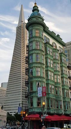 a tall green building sitting on the side of a street next to tall buildings with windows