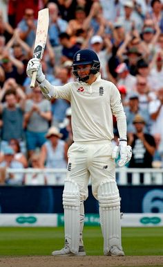 a man holding a cricket bat on top of a field in front of a crowd