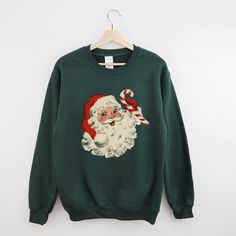 Vintage Santa Christmas Sweatshirt  Check out our other Christmas Sweatshirts & TShirts here -> https://etsy.me/3wHQxlY  Details: * Unisex Cotton Blend Crewneck Sweatshirt * Loose Fit  * Pre-Shrunk  * Machine Washable  * Unisex Fit - Refer to sizing guide in photos for sizes  Care Instructions *PLEASE READ*  * Cold machine wash only on a gentle cycle with similar colours - wash garment inside out  * Use standard washing powder only; it is not recommended that fabric softeners be used as they may strip the coloured ink * If ironing is necessary, iron inside-out on the lowest setting (do not iron directly onto print). * Garment can be tumble-dried on a low cycle, but hang-dry works best * Do not use bleaching agents * Do not dry clean  Returns policy: We don't accept returns or exchanges. Bu Holiday Sweatshirts, Sweatshirts Vintage, Sweat Vintage, Plus Size Christmas, Christmas Apparel, Santa Sweatshirt, Crewneck Vintage, Retro Sweatshirts, Christmas Crewneck