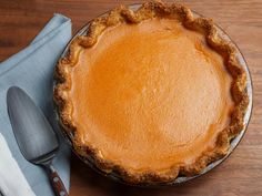 a pie sitting on top of a wooden table next to a knife and fork,