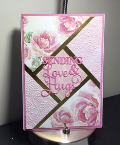 a close up of a greeting card on a metal stand with flowers and the words sending loves hugs