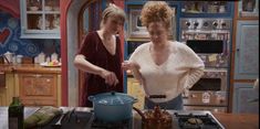 two women standing in a kitchen preparing food on top of a stove and an oven