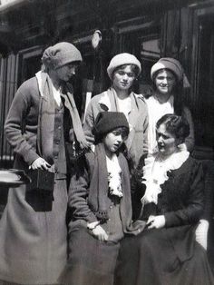 an old black and white photo of four women standing next to each other in front of a train