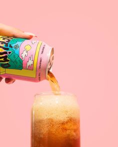 a person is pouring something into a glass with some liquid in it on a pink background