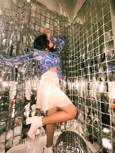 a woman standing on top of a toilet in front of a mirror tiled bathroom wall