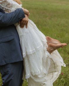 a man in a suit and tie holding a woman's dress while standing on a lush green field