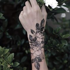 a woman's arm with flowers on it and leaves around her wrist, in front of some bushes