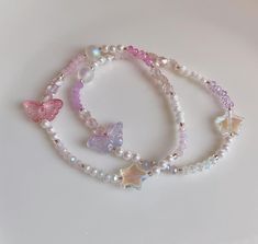 three bracelets with butterfly charms and pearls on them sitting on a white table top