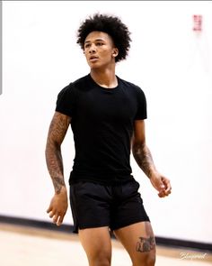 a man standing on top of a basketball court with a ball in his hand and tattoos on his arm