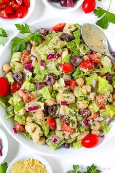 a salad in a white bowl with olives, tomatoes and lettuce on the side