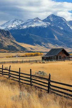 an old barn sits in the middle of a grassy field with mountains in the background