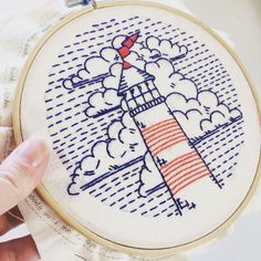 a hand is holding up a cross stitch pattern with a lighthouse in the sky on it