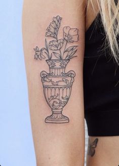 a woman with a tattoo on her arm has a vase full of flowers in it