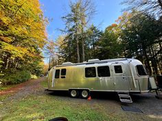 an airstream parked on the side of a road in front of trees with leaves