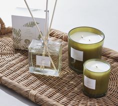 three candles sitting on top of a wicker tray next to a box with a candle in it