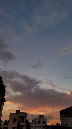 the sun is setting behind some buildings and clouds in the sky, with an airplane flying overhead