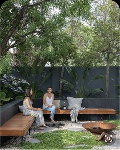 two women sitting on benches in the middle of a garden with fire pit and seating