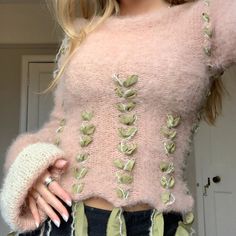 a woman wearing a pink sweater with green leaves on it