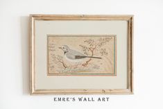 a bird sitting on top of a white wall next to a framed painting above it