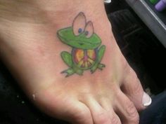 a person with a tattoo on their foot that has a frog holding a peace sign