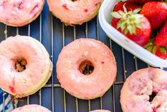 strawberry donuts with icing and strawberries on a cooling rack next to a bowl of strawberries