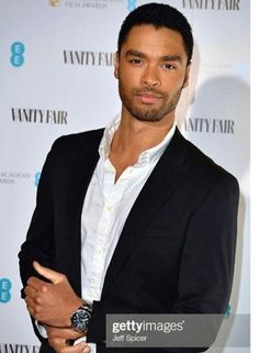 a man in a black suit and white shirt posing for the camera with his arms crossed