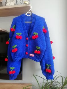 a blue sweater with red cherries on it hanging from a hook next to a potted plant