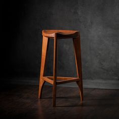 a wooden stool sitting on top of a hard wood floor next to a gray wall