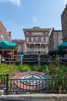 an outdoor seating area with tables and umbrellas in front of a brick building on a sunny day