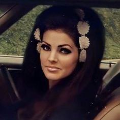 a woman sitting in the back seat of a car with long dark hair and flowers on her head