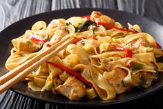 a black plate topped with pasta and chopsticks on top of a wooden table