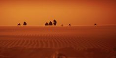 a group of people sitting on top of a sandy hill in the middle of the desert