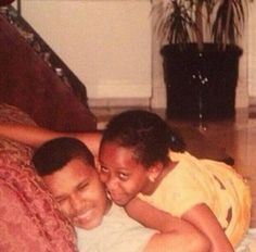 two children laying on top of each other in front of a couch with their arms around one another