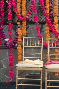 two chairs with pink and orange flowers hanging from the ceiling next to each other in front of a stone wall