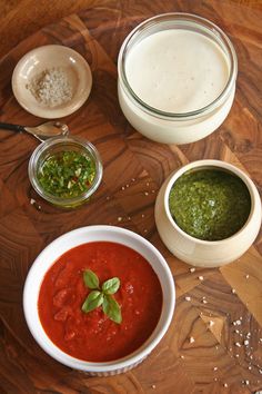 three bowls of soup on a wooden table with pesto and breadcrumbs