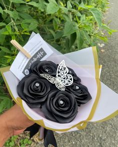 a person holding a bouquet of black roses with a butterfly brooch in it's center