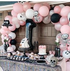 a table topped with lots of pink and black balloons next to a giant balloon arch