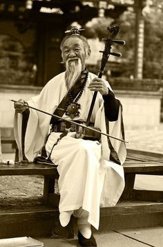 an old man is sitting on a bench with his instrument in hand and smiling at the camera