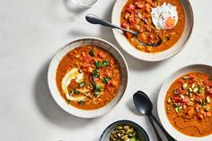 three bowls of soup on a white table with spoons and silver utensils