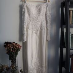 a white dress hanging on a rack next to a book shelf and vase with flowers