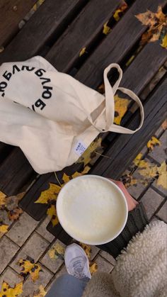 a person sitting on a bench next to a white bag and a bowl of milk