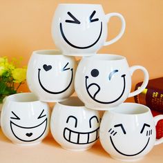 four coffee mugs with faces drawn on them sitting next to a book and flowers