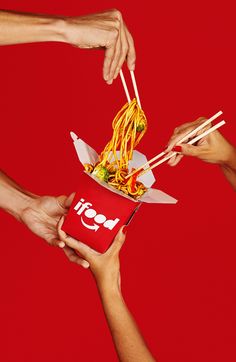 four people holding chopsticks over a box of noodles