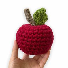 a hand holding a crocheted apple with a green leaf on the top and bottom