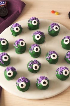 green and purple cookies with googly eyes on a white plate next to candy candies