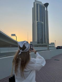 a woman taking a photo with her cell phone in front of a tall building at sunset