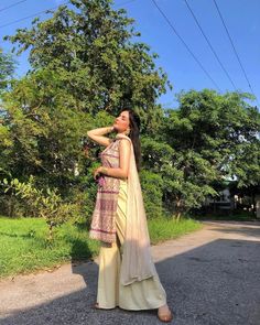 a woman standing on the side of a road wearing a yellow and pink lehenga