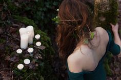 a woman standing next to a tree with candles in it's back and greenery around her